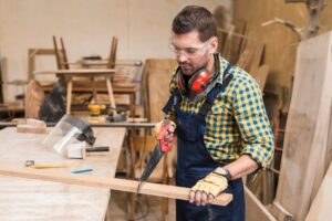 professional-carpenter-cutting-wooden-plank-with-handsaw-workshop