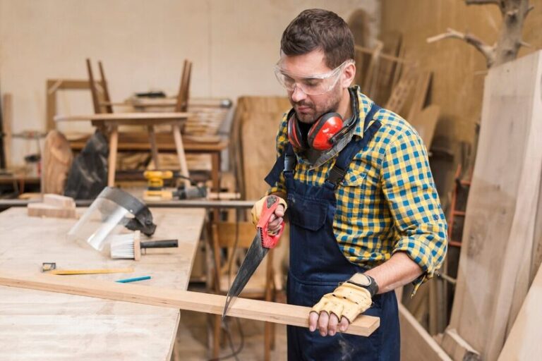 professional-carpenter-cutting-wooden-plank-with-handsaw-workshop